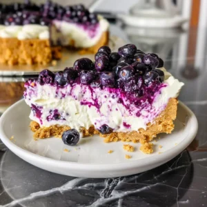 A slice of no-bake blueberry cheesecake on a white plate, with a bite taken out.