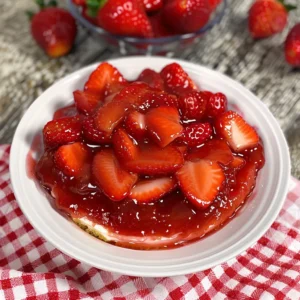 Bowl of homemade strawberry topping for cheesecake, surrounded by fresh strawberries.